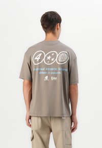 Grå bomulds t-shirt med et stort grafisk motiv bagpå, der inkluderer tekst, stjerner og et globusdesign. Den har korte ærmer og en afslappet pasform.