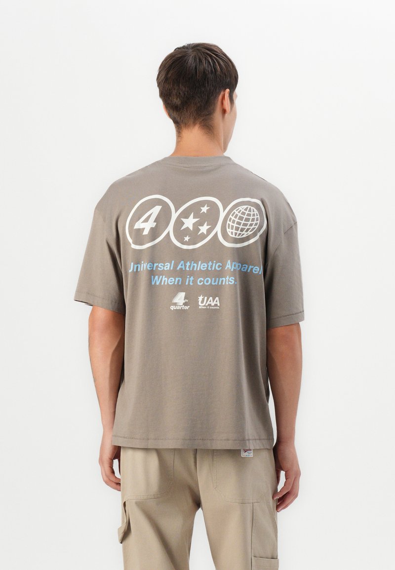 Grå bomulds t-shirt med et stort grafisk motiv bagpå, der inkluderer tekst, stjerner og et globusdesign. Den har korte ærmer og en afslappet pasform.