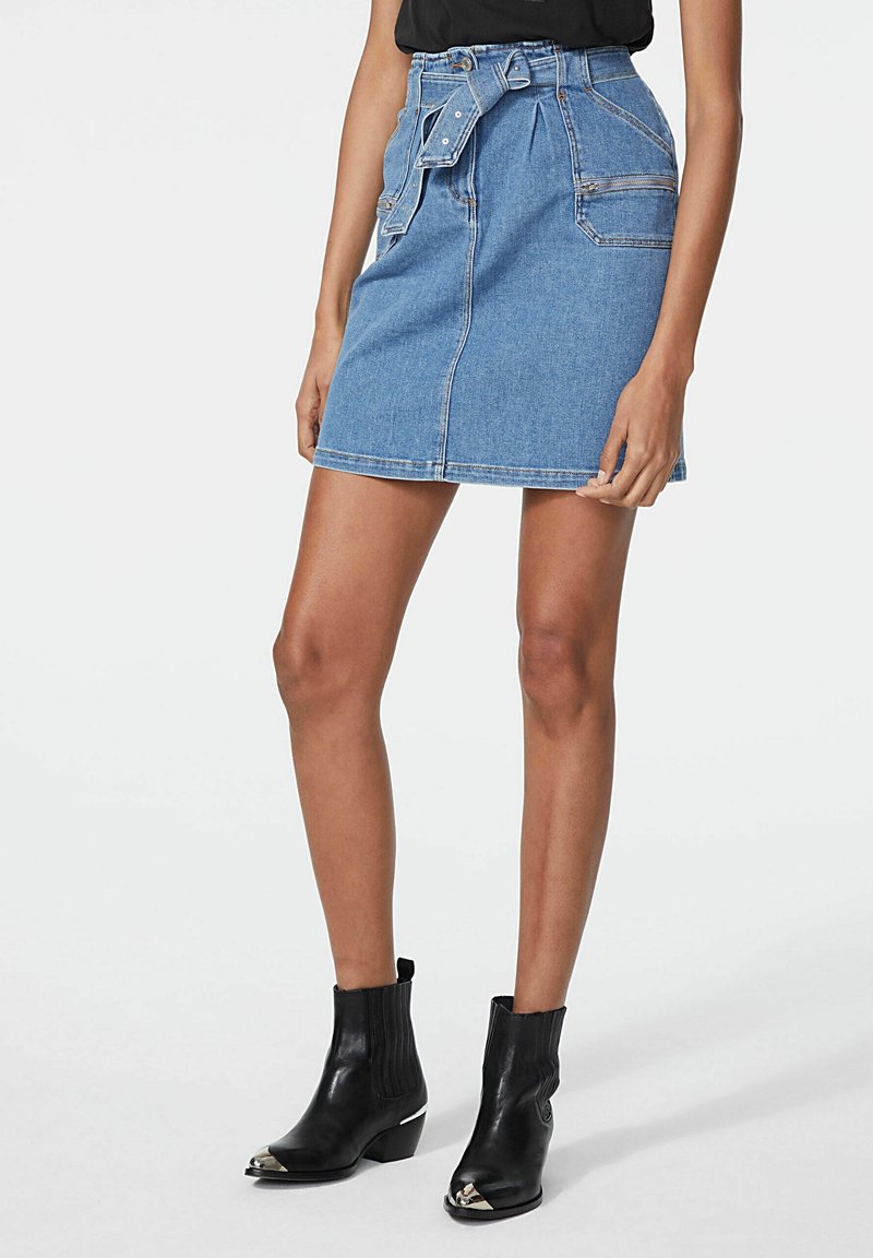 Džínová sukně se páskem v pase, se bočními kapsami a klasickou modrou barvou. V kombinaci s černými kotníkovými botami se stříbrnými akcenty.