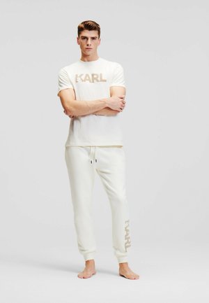 Witte katoenen t-shirt met "KARL" opdruk in beige, gecombineerd met lichtbeige geribde joggingbroek met een soortgelijk logo op het been.