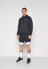 Marine hoodie med en frontlomme og logodetalje, parret med sorte shorts over hvide atletiske tights, komplet med sorte sneakers og hvide sokker.