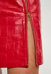 Rød faux læderskirt med krokodillemønster, en sideguldlynlås og et højt slidser, der forbedrer dets slanke geometriske design.