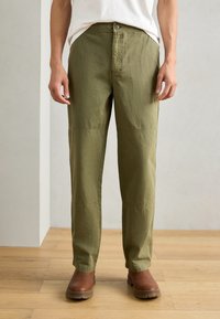 Olive green pants with a straight cut, featuring a front button closure, side pockets, and subtle knee paneling. Worn with brown boots.