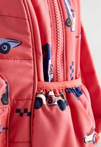 Veste rembourrée rose corail ornée d'impressions de voitures de course en cartoon, avec une fermeture éclair sur le devant, des accents élastiques et des détails froncés au bas de l'ourlet.