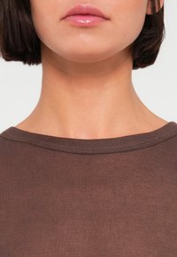 Καφέ τοπ με ριμπ υφή, φαρδύ ντεκολτέ, λεία υφή και εφαρμοστή γραμμή, τονίζοντας την περιοχή του γιακά και των ώμων.