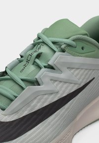 Hellgrüner und weißer Sportschuh mit schwarzem Nike-Swoosh, Mesh-Obermaterial, Zickzack-Design nahe den Schnürsenkeln und Schriftzug "VAPOR PRO" auf der Zunge.