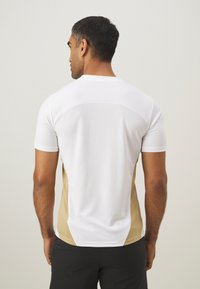 Maglietta sportiva da uomo realizzata in tessuto bianco con pannelli laterali beige, maniche corte e design aderente. Materiale testurizzato per una maggiore traspirabilità.