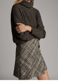 Maglione marrone oversize con collo alto realizzato in materiale morbido, abbinato a una gonna mini a vita alta con un dettaglio a bottoni.