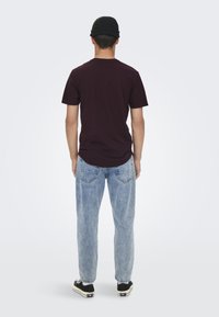 Maroon short-sleeve shirt, light blue loose-fitting jeans, black shoes with white accents, and a black beanie, viewed from the back.