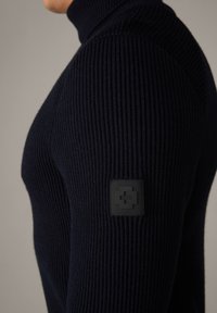 Maglione a collo alto a coste navy realizzato in tessuto testurizzato, con una patch quadrata nera con marchio sulla parte superiore del braccio.