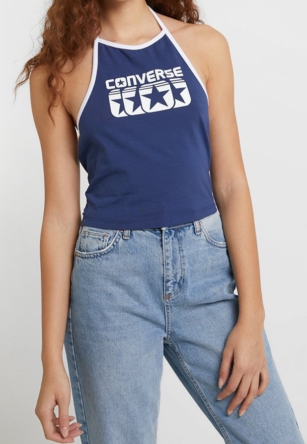 Granatowy top na halter z białym wykończeniem i grafiką "Converse" na środku; zestawiony z jasnoniebieskimi spodniami o wysokim stanie.