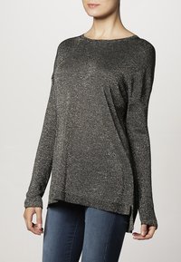 Haut noir à manches longues en tissu texturé et brillant. Présente un décolleté rond et des fentes sur les côtés pour un ajustement décontracté.