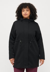 Manteau noir à capuche avec fermeture éclair à l'avant, deux poches avant, détails froncés et un tissu doux et texturé. Conçu pour le confort et la chaleur.
