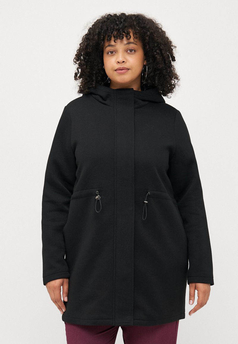 Manteau noir à capuche avec fermeture éclair à l'avant, deux poches avant, détails froncés et un tissu doux et texturé. Conçu pour le confort et la chaleur.