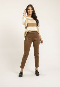 Pull en tricot beige et beige rayé avec encolure bateau, associé à un pantalon ajusté marron et des mocassins noirs épais. Tissu simple et texturé.