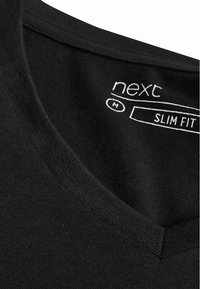Fekete, slim fit V-nyakú póló. Puha, bordázott textúrával rendelkezik, és a belső nyakrészen nyomtatott márkajelzés található.