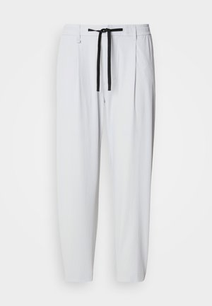 Biele zúžené nohavice s čiernym šnúrkovým pásom, elastickým pásom, bočnými vreckami a pútkami na opasok, zobrazené na jednoliatom pozadí.