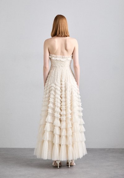 Robe sans bretelles, de couleur crème, faite de tulle superposé avec des accents en volants. Design à tiers sur toute la longueur, créant une apparence texturée.