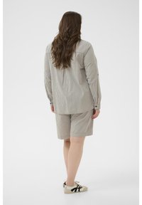 Chemise à rayures boutonnée avec manches longues assortie à un short rayé dans des tons discrets. Le mannequin porte des baskets décontractées.