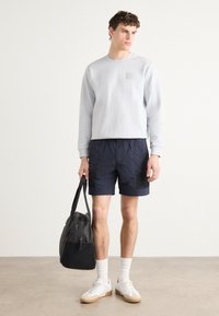 Svetle šedá mikina se strukturovaným povrchem, námořnické kraťasy, bílé ponožky, bílé tenisky a černá taška se zipem. Jednoduchý design a ležérní vzhled.