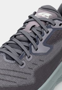 Chaussure de sport grise avec une tige en mesh texturé, un système de laçage flexible et une semelle en caoutchouc vert menthe avec une semelle intermédiaire rembourrée.