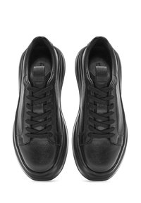Sneaker in pelle nera con superficie testurizzata, lacci piatti e suola in gomma spessa. Caratterizzate da un design minimalista e una forma arrotondata e liscia.
