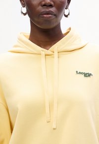 Felpa gialla con una texture morbida, caratterizzata da un sottile logo Lacoste ricamato, cordini e un classico design con tasca a marsupio.