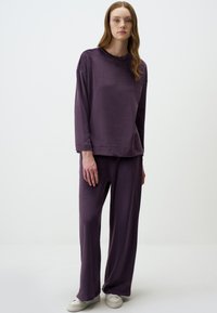 Set di abbigliamento da casa viola realizzato in tessuto morbido; presenta una maglietta a maniche lunghe con girocollo e taglio rilassato, abbinata a pantaloni a gamba ampia.