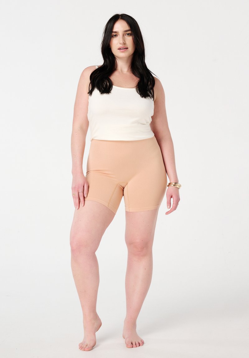 Shorts en stretch beige au design ajusté, associés à un débardeur crème. Le tissu semble doux, avec une texture lisse et des coutures minimales.