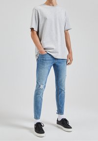 Grå bomullströja i kombination med ljusblå slitna jeans. Jeanserna har revor och en tapered passform. Svarta sneakers med vita sulor fulländar outfiten.