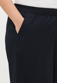 Zwarte elastische taillebandbroek met zijzakken; gladde textuur en losse pasvorm. Geen zichtbare patronen of hardware.