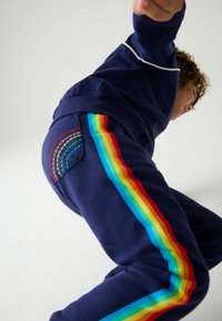 I pantaloni della tuta blu navy presentano strisce arcobaleno lungo i lati e cuciture colorate sulla tasca posteriore, realizzati in un morbido tessuto misto.