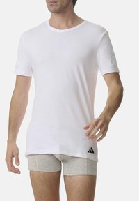 White short-sleeve T-shirt made of cotton with a round neckline. Features a black Adidas logo at the lower side. Worn over gray boxer shorts.