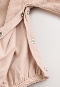 Close-up of beige fabric with three metal snap buttons and elastic seam, showing part of a garment opening.