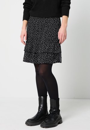 Jupe noire à fleurs avec des volants superposés, ornée d'un petit motif de fleurs blanches. Associée à des collants noirs et des bottines noires à semelles épaisses.