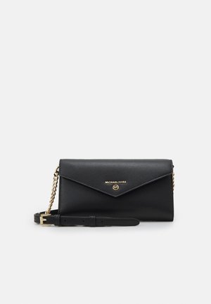Pochette en cuir noir Michael Kors avec chaîne dorée, rabat enveloppe et logo sur le devant, sur fond gris clair.