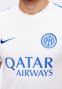 Λευκή αθλητική φανέλα με μπλε λογότυπο Nike, έμβλημα της Ίντερ Μιλάνο και κείμενο χορηγού Qatar Airways στο στήθος.