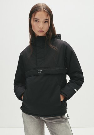 Geacă neagră tip windbreaker cu guler înalt, buzunar frontal și șnururi ajustabile la talie și la tiv. Materialul pare neted și ușor.