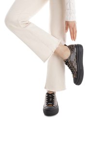 Zapatillas de plataforma negras con un diseño de estampado animal en tonos marrones y negros, con cordones negros y suelas de goma texturizadas, combinadas con pantalones claros cortos.