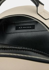 Interior de bolso de cuero beige con forro negro, que presenta un zip plateado y una etiqueta interior que dice "A/X ARMANI EXCHANGE."