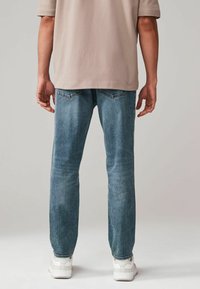 Jeans din denim de culoare albastră deschisă, cu o croială drept, având buzunare spate și detalii minime, purtate cu o cămașă bej și adidași albi.