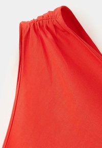 Gros plan d'une manche en tissu rouge avec un élastique rassemblé au bord supérieur, montrant une texture lisse et des coutures soignées.