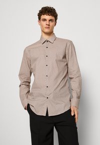 Camicia con bottoni a maniche lunghe, caratterizzata da un motivo geometrico in beige e marrone, colletto a punta e bottoni neri, realizzata in tessuto liscio.