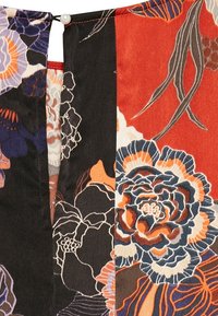 Tessuto floreale con colori vivaci di nero, rosso e crema, caratterizzato da motivi dettagliati di fiori e foglie. Accentuato con un bottone di perla.