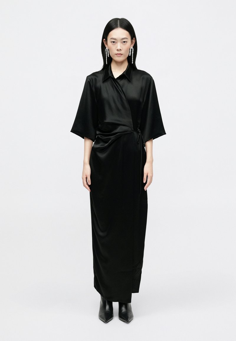 Vestido envolvente de satin negro com colarinho e mangas largas, apresentando um detalhe de cintura laçada, combinado com botas de tornozelo de salto triangular.