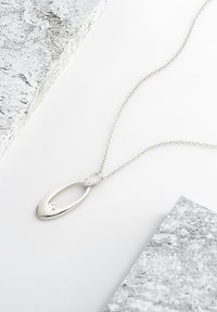 Sølv vedhængs halskæde med et ovalt design, prydet med en lille diamantaccent og et tekstureret oval detaljer, hængende på en delikat kæde.