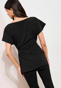 Sort top med korte, brede ærmer og en tætsiddende talje. Glat, mat stof med en lige, let løs silhuet ved kanten.