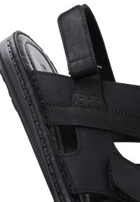 Sandal de cuero negro con correa ajustable, plantilla acolchada y acentos de costura. Diseño abierto con recortes laterales para transpirabilidad.