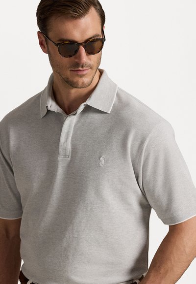 Svetlo siva polo majica z teksturiranim tkanjem in kratkimi rokavi, ki na prsih nosi majhen vezen logo. Ovratnik je rahlo odprt.