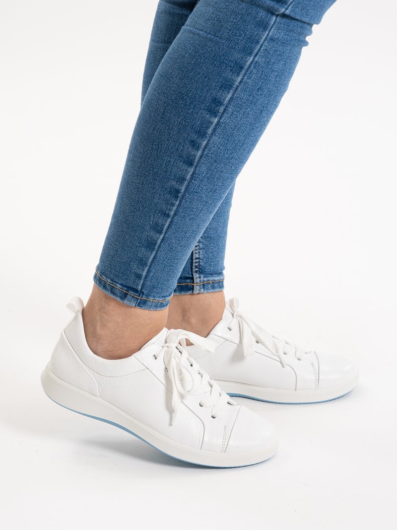 Persona con vaqueros ajustados azules y zapatillas de cuero blancas con cordones y suelas azul claro sobre fondo blanco.